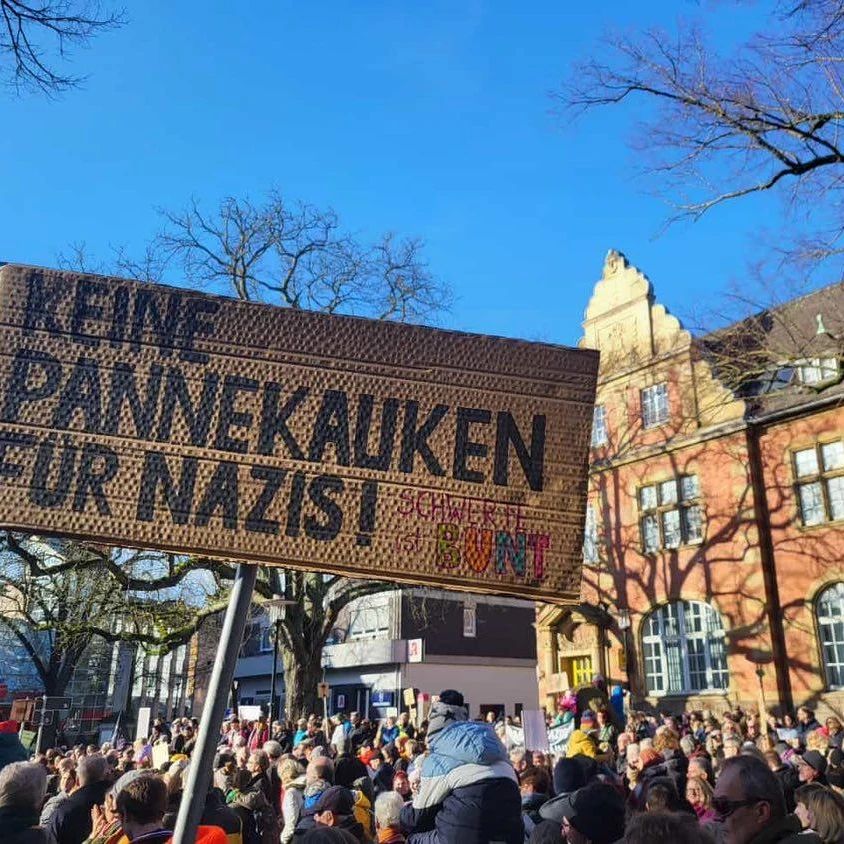 Ganz viele Menschen auf dem Postplatz, im Hintergrund die Post. Einige tragen Schilder. Im Vordergrund ist ein Schild mit der Aufschrift "Keine Pannekauken für Nazis -n Schwerte ist bunt" zu erkennen,