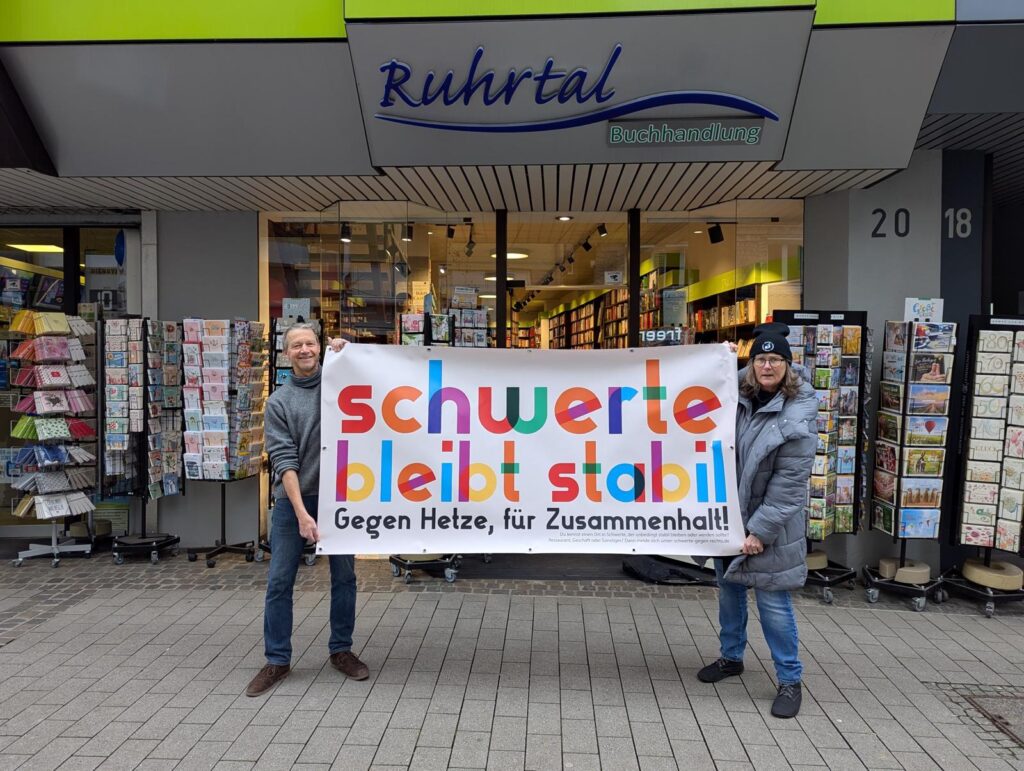 Jörg Schröder und Heike Liefländer-Gruner stehen mit einem Bannner mit Kampagnen-Logo vor der Ruhrtal-Buchhandlung