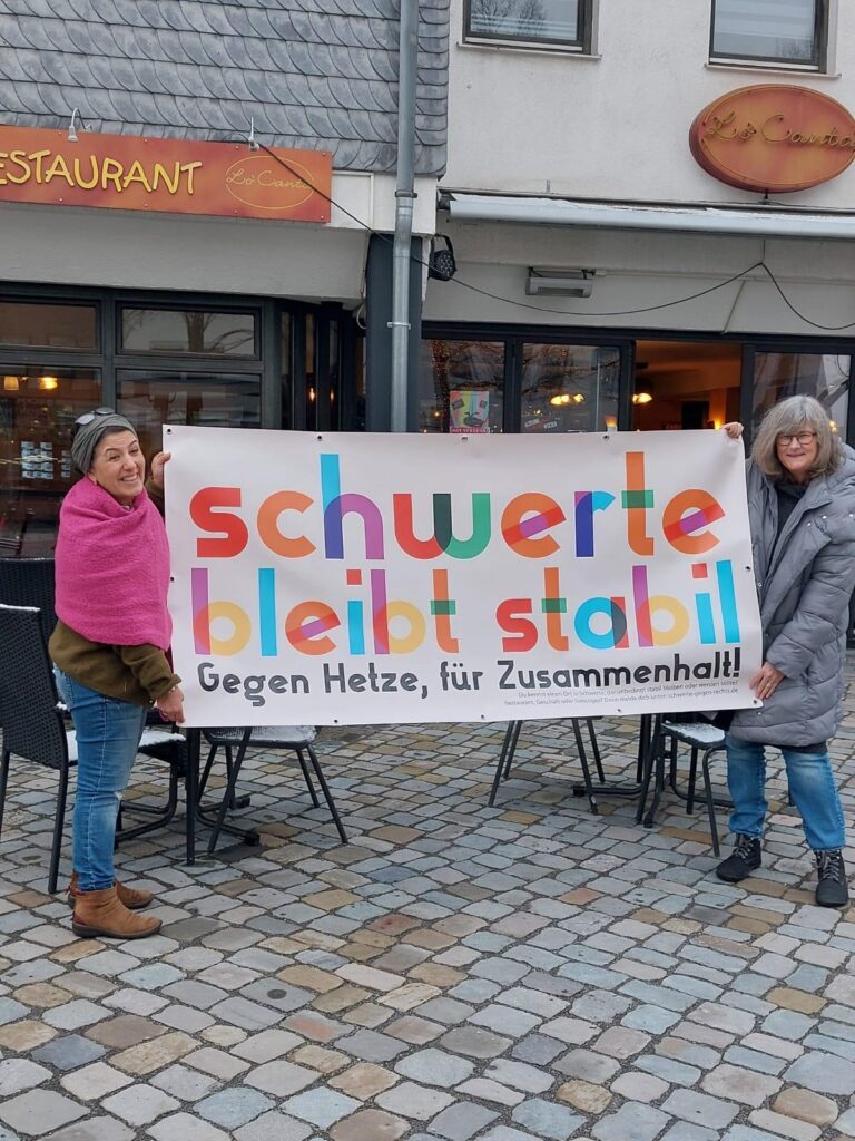 Ayse Yilmaz und Heike Liefländer-Gruner stehen mit einem Bannner mit Kampagnenlogo vor dem Restaurant Lo Canta