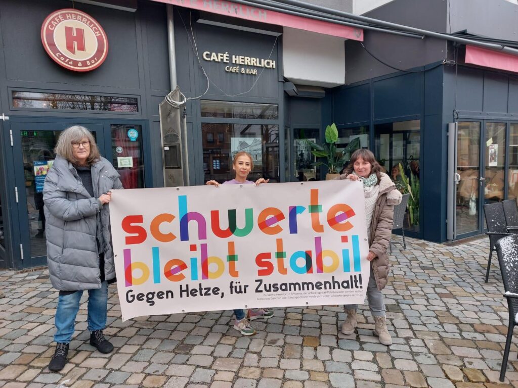 Andrea Parnow, Sivita Karakus und Heike Liefländer-Gruner stehen mit einem Bannner mit Kampagnenlogo vor dem Cafe Herrlich