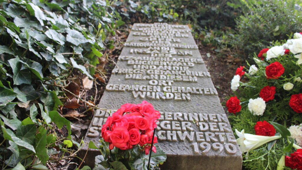Vor dem Gedenkstein mit der Aufschrift "Zur Mahnung an die Gegenwart und zum Gedenken an die Opfer des Nationalsozialismus an die Insassen des KZ-Außenlagers Buchenwald und an die Kriegsgefangenen die an diesem Ort gefangen gehalten wurden - Bürgergerinnen und Bürger der Stadt Schwerte 1990" stehen rote Blumen.